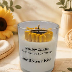 May include: A clear glass candle container filled with white wax, featuring a yellow sunflower-shaped wax topper and a central wick. The label reads: Soha Soy Candles, Hand Poured Soy Candle, Sunflower Kiss, in black text on the front surface.