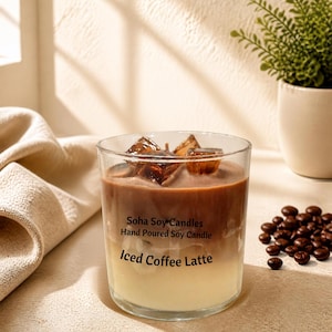 May include: A clear glass candle shaped like an iced coffee latte with two distinct layers of wax, dark brown on top and cream on the bottom. The top features brown wax ice cubes. The label reads Soha Soy Candles Hand Poured Soy Candle Iced Coffee Latte.