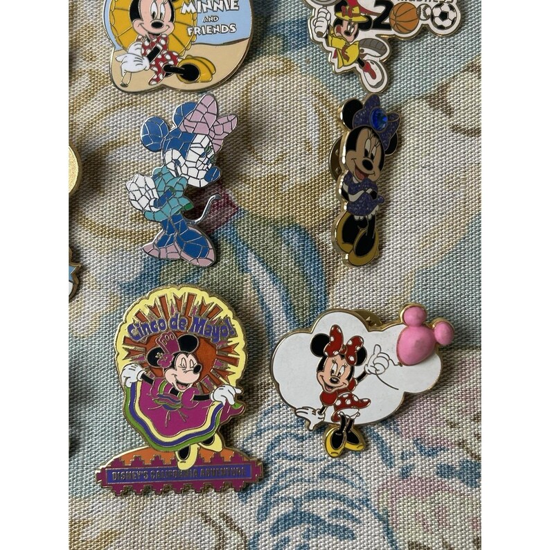 May include: A collection of Disney character pins featuring Mickey and Minnie Mouse. The pins showcase various designs, including Minnie in a Cinco de Mayo outfit and Mickey with a soccer ball. The pins are colorful and detailed, with a variety of shapes and sizes.