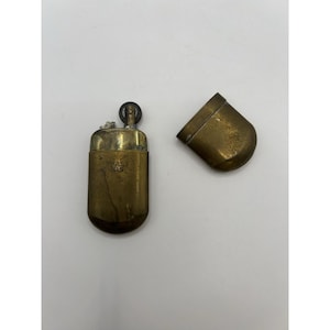 Puede incluir: Un encendedor de lat&oacute;n vintage con tapa extra&iacute;ble, que presenta una forma rectangular redondeada y un acabado de metal texturizado. El cuerpo del encendedor est&aacute; grabado con el texto BRASS No5 e incluye una rueda de encendido circular.
