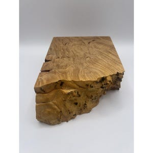 Peut inclure: Un bloc de bois rectangulaire brun clair avec une surface naturelle et texturée. Le grain du bois présente des motifs tourbillonnants et des nœuds, avec un bord rugueux et irrégulier d'un côté. Le bloc semble être une coupe transversale d'un tronc d'arbre.