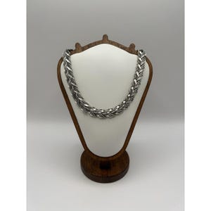 May include: A silver-toned necklace featuring a repeating herringbone or chevron link pattern. The metal links have a textured, oxidized finish that highlights the intricate, angled design of each individual segment throughout the chain.