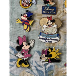 May include: A collection of Disney character pins featuring Mickey and Minnie Mouse. The pins showcase various designs, including Minnie in a pink dress and a pin with the text "Walt Disney World, The Happiest Celebration On Earth".
