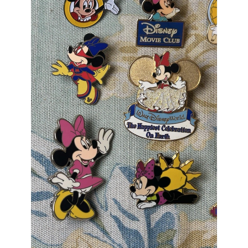 May include: A collection of Disney character pins featuring Mickey and Minnie Mouse. The pins showcase various designs, including Minnie in a pink dress and a pin with the text "Walt Disney World, The Happiest Celebration On Earth".