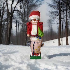 Op de afbeelding: Een houten notenkrakerfiguur gekleed in een rode jas en muts met een witte imitatiebontbaard. Het figuur draagt een beige zak gevuld met klein speelgoed, waaronder een groene boom, en staat op een groene rechthoekige voet.