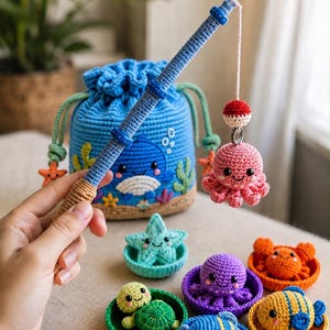 May include: A blue crochet drawstring bag featuring a whale design, accompanied by a crochet fishing rod with a pink octopus lure. Several small crochet sea creatures, including a turtle, crab, and fish, sit in individual colourful bowls.