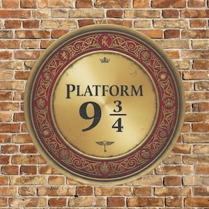 Puede incluir: Letrero metálico redondo de color dorado con el texto "PLATFORM 9 3/4" en negro. El letrero tiene un borde rojo decorativo con diseños ornamentados y está colgado en una pared de ladrillo.
