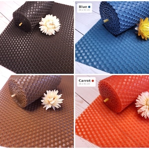 May include: A collection of four rectangular beeswax sheets in black, blue, brown, and carrot orange, each featuring a hexagonal honeycomb pattern. Each sheet measures 26 by 41 cm and is accompanied by a single dried white flower blossom.