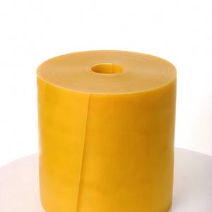 May include: A cylindrical roll of smooth, opaque, golden-yellow rubber material. The roll features a consistent, solid color throughout its surface and a hollow circular center opening, standing upright with a clean, continuous edge visible.
