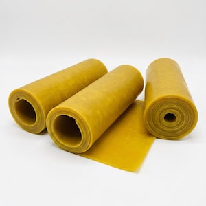 Könnte beinhalten: Drei Rollen aus flexiblem, senfgelbem Gummimaterial. Die Rollen sind zylindrisch geformt und haben eine glatte, matte Textur. Eine Rolle ist teilweise abgerollt und zeigt ein flaches, rechteckiges Blatt aus demselben gelben Gummimaterial.