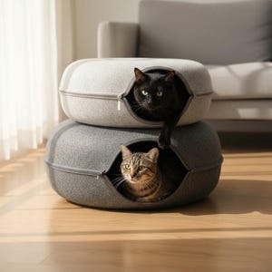 May include: Two stacked circular pet beds made of felted material, one light gray and one dark gray. Each bed features a zippered opening. A black cat is emerging from the top light gray bed, while a brown tabby cat sits inside the bottom bed.