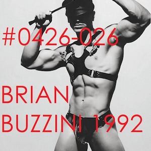 May include: A black leather harness with metal buckles and rings, a matching leather cap, and a leather jockstrap. The image features the red text #0426-026, BRIAN, and BUZZINI 1992 overlaid on the black and white photograph of the leather gear.