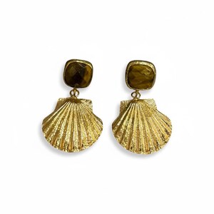 May include: A pair of gold-toned earrings featuring a faceted, square-shaped brown gemstone at the top, connected by a small metal loop to a textured, fan-shaped seashell pendant with a metallic gold finish and distinct vertical ridges.