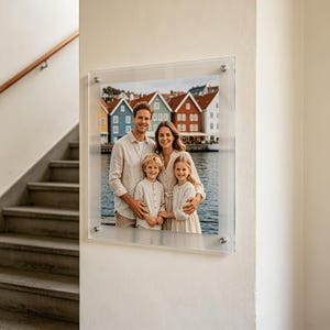 May include: A rectangular clear acrylic photo frame mounted on a wall, featuring a photograph of a family of four standing in front of colourful waterfront buildings. The frame is secured with four silver metal standoffs at each corner.