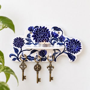 May include: A cloud-shaped ceramic wall shelf featuring a blue and white floral pattern. The shelf includes a small horizontal ledge holding a lit tea light candle and three hooks underneath, each supporting an antique-style brass skeleton key.