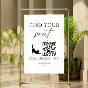Puede incluir: Un cartel rectangular blanco para el plan de asientos de una boda colgado de un soporte de metal dorado. El cartel presenta el texto negro FIND YOUR SEAT, una silueta de gato negro, un código QR, el texto SCAN. SEARCH. SIT. y los nombres Emma & Michael con 08.15.26.