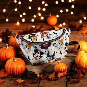 May include: A white fanny pack featuring a repeating pattern of Disney characters dressed in Halloween costumes, including Mickey Mouse as a vampire and Goofy as a pumpkin, accented with small black bats and orange stars, finished with a black zipper.