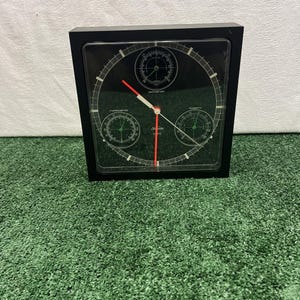 May include: A square black wall clock featuring a black face with white markings, three red hands, and three smaller circular gauges labeled barometer, thermometer, and humidity. The brand name Sunbeam Quartz is printed in white on the clock face.