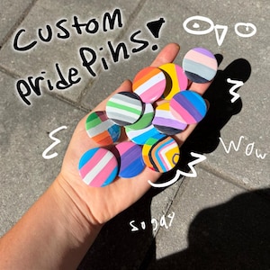 May include: A collection of circular pins featuring various colorful striped patterns representing different pride flags. The text Custom pride Pins! is written in black, with additional white hand-drawn doodles and the words wow and so gay.