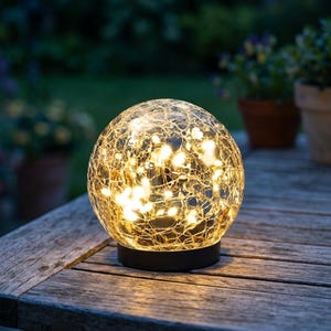 May include: A spherical glass lamp with a crackled texture, illuminated from within by warm white string lights. The globe sits on a circular black base, creating a glowing effect that highlights the intricate web of fractures across the surface.