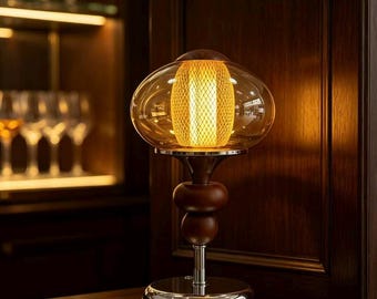 May include: A table lamp featuring a rounded amber glass shade with a central gold mesh cylinder. The base consists of two stacked dark brown wooden spheres atop a polished chrome stem and a circular chrome base with a small black power switch.