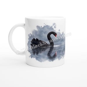 May include: A white ceramic mug featuring a printed image of a black swan swimming on calm water with a soft gray watercolor-style background. The text TheBlackSwanSisters is printed in a dark font across the center of the mug.