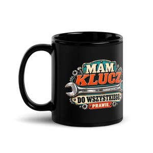 Peut inclure: Un mug en céramique noir orné d'un motif graphique représentant une clé plate argentée et le texte "MAM KLUCZ DO WSZYSTKIEGO. PRAWIE.". Le design inclut des éléments mécaniques comme des engrenages et des boulons en bleu, orange et blanc.
