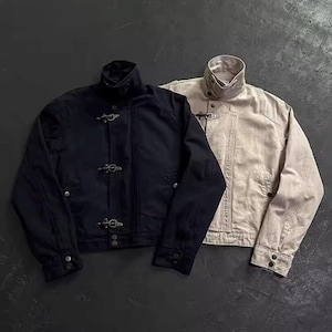 Könnte beinhalten: Zwei Jacken, eine in Schwarz und eine in Beige, mit hohem Kragen, Druckknopfverschlüssen und drei metallenen Feuerwehr-Verschlüssen an der Vorderseite. Jede Jacke hat lange Ärmel mit Druckknopfmanschetten und eine strukturierte, kurze Passform.