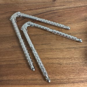 May include: Two silver-colored metal nutcrackers with textured, patterned handles. Each tool features a hinged design with a central pivot point and long, slender arms that have a repeating decorative embossed pattern along their entire length.