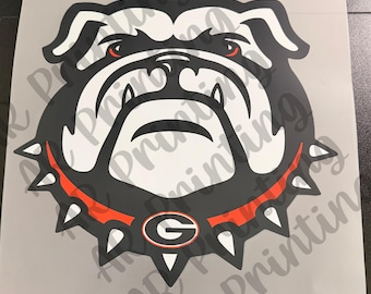 May include: A graphic decal featuring the stylized head of a bulldog with black, white, and red coloring. The bulldog wears a spiked red collar with a central black and white letter G emblem. The design is printed on a light gray square sheet.