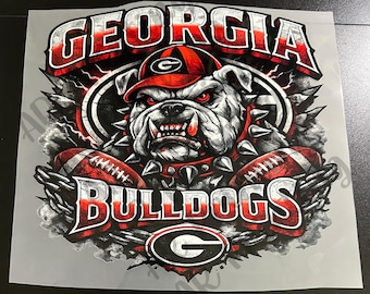 May include: A graphic transfer featuring a snarling bulldog wearing a red and black cap with a G logo. The text GEORGIA appears above and BULLDOGS below, with two footballs, a spiked collar, and a large G logo at the bottom in red, white, and black.