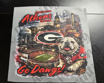 May include: A graphic transfer sheet featuring a collage of Athens, Georgia landmarks, a football stadium, a red and black Georgia G logo, and a bulldog wearing a red jersey with a spiked collar, with the text Downtown Athens Georgia and Go Dawgs.