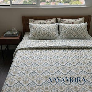 May include: A bed featuring a duvet cover and two matching pillows with a repeating scalloped floral pattern in muted shades of blue, green, and tan. The bed has a wooden headboard and is positioned in a room with a large window. The text AAYAMORA is visible.