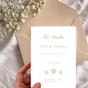 May include: A white rectangular save the date card featuring the text The Smiths, Lily & Thomas, SAVE THE DATE, 29.05.2027, Fingal Bay, NSW, and Formal Invitation to Follow, decorated with three small seashell illustrations above the location text.