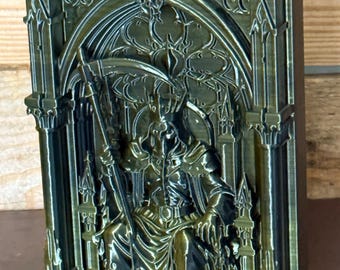 May include: A rectangular metallic bronze-colored plaque featuring a high-relief sculpture of a cloaked figure wearing a crown and holding a scythe. The figure sits on a throne within a gothic archway, flanked by pillars and skulls at the base.