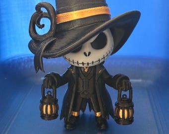 May include: A stylized figurine of a skeletal character wearing a black top hat with an orange band and a black coat. The character has a white skull face with black eye sockets and a stitched mouth, holding a small black lantern in each hand.