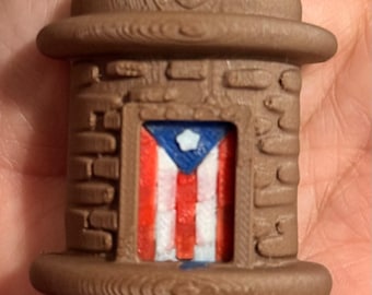 May include: A brown, three-dimensional, cylindrical object with a textured surface resembling stone masonry. It features a central rectangular inset displaying the flag of Puerto Rico, characterized by red and white stripes, a blue triangle, and a white star.
