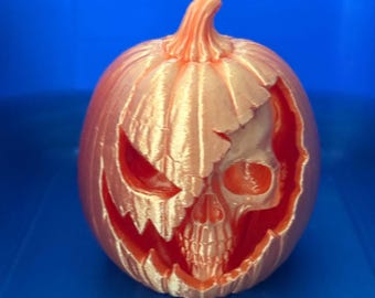 May include: A metallic orange pumpkin sculpture featuring a carved-out section that reveals a detailed human skull underneath. The pumpkin has a textured, ribbed surface with a jagged opening, showcasing a realistic skeletal face with eye sockets.