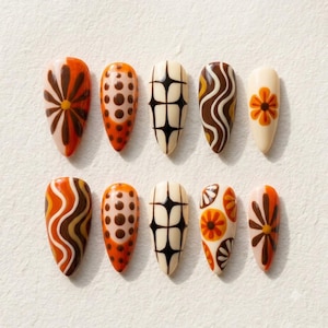 May include: A set of ten almond-shaped press-on nails featuring a retro-inspired color palette of cream, orange, and dark brown. The designs include floral patterns, wavy lines, polka dots, and geometric starburst shapes arranged in two rows.