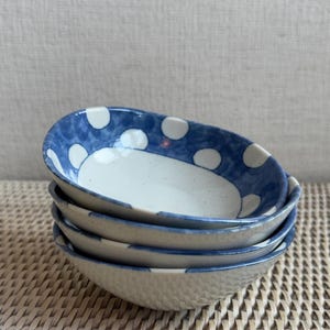 May include: Four stacked white ceramic bowls with a blue and white polka dot design.