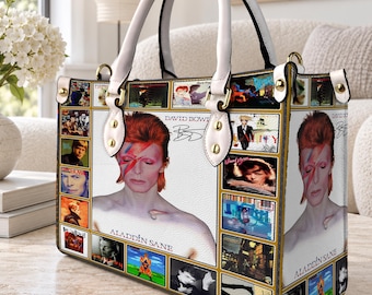May include: A rectangular handbag featuring a collage of David Bowie imagery, including the Aladdin Sane album cover with the iconic lightning bolt makeup. The bag has white top handles, gold-tone hardware, and a white base with printed text.