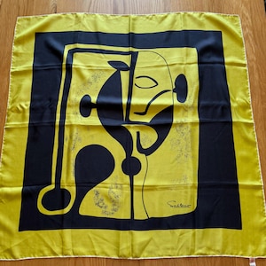 May include: A square scarf featuring a bright yellow border and a central black graphic print of an abstract face. The design includes black lines and shapes on a yellow background with a signature reading Saltino in the bottom right corner.