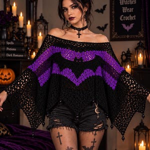 May include: A black and purple off-the-shoulder crochet poncho featuring a bat motif across the chest, wide bell sleeves, and a pointed hemline with dangling black beads. The garment is worn with black distressed denim shorts and a cross choker.