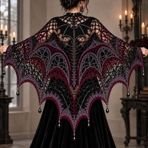 May include: A black, dark red, and purple crocheted shawl featuring a bat-wing design with intricate web-like patterns. The garment is adorned with small, dangling black teardrop-shaped beads along the scalloped bottom edge.