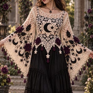 May include: A cream-colored crochet top with wide bell sleeves, featuring black crescent moon and star motifs, dark purple floral accents, and dangling tassels. The top is layered over a black dress with a tiered, ruffled skirt and lace trim.