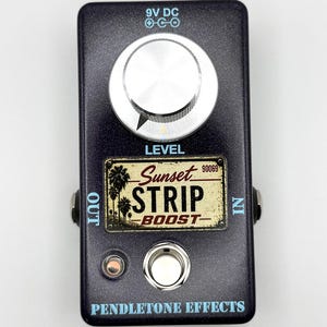 May include: A dark metallic purple guitar effects pedal featuring a large silver knob labeled LEVEL, a footswitch, and a rectangular graphic plate reading Sunset STRIP BOOST 90069 with palm trees. The pedal is labeled PENDLETONE EFFECTS.