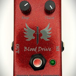 May include: A red glittery guitar effects pedal labeled Blood Drive with two black control knobs marked Rage and Thirst. The center features a graphic of a dagger with wings. Text includes 9V DC, OUT, IN, and PENDLETONE EFFECTS with a green LED.