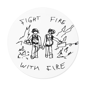 May include: A circular white sticker featuring a black line drawing of two figures in vests holding equipment amidst flames. The text "FIGHT FIRE" is written above the figures, and "WITH FIRE" is written below them in a hand-drawn style.