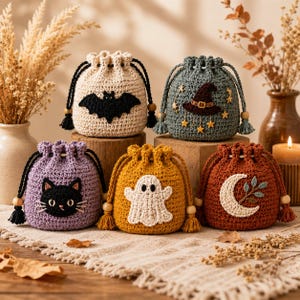 May include: Five small, round, crocheted drawstring pouches in cream, dark green, lavender, mustard yellow, and burnt orange. Each pouch features a unique applique: a black bat, a brown witch hat with stars, a black cat face, a white ghost, and a crescent moon.