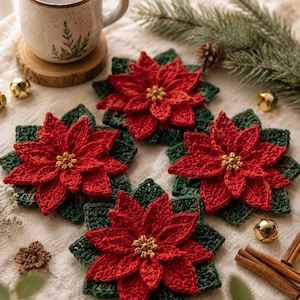 May include: Four square crochet coasters featuring a three-dimensional red poinsettia flower with a gold center, layered over a dark green leaf base. The coasters are arranged on a textured fabric surface alongside a ceramic mug and pine sprigs.